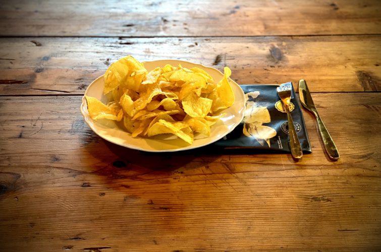 Des chips à la truffe dans une assiette blanche posée sur un plan de travail en bois